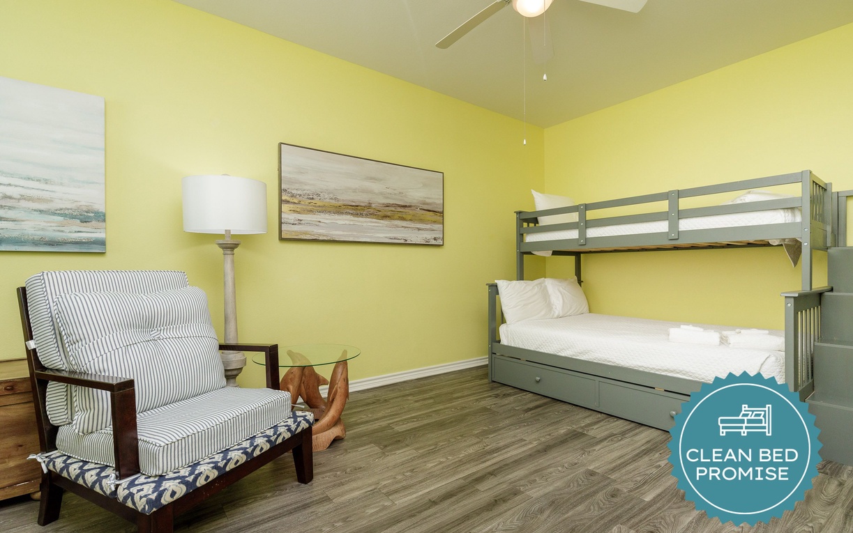 Your cheerful yellow bedroom features a cozy bunk bed and reading chair with coastal artwork for relaxing family stays.