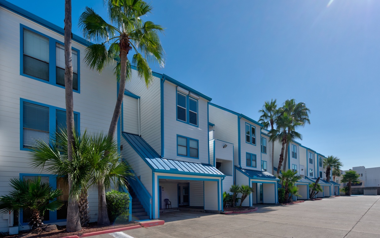 Modern vacation rental complex featuring blue-trimmed buildings surrounded by tropical palms under clear sunny skies.