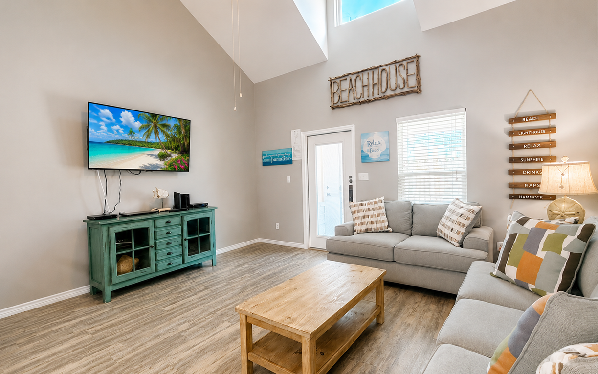 Kick back in the inviting living room with comfortable seating, a wall-mounted TV, and a bright, airy coastal atmosphere.