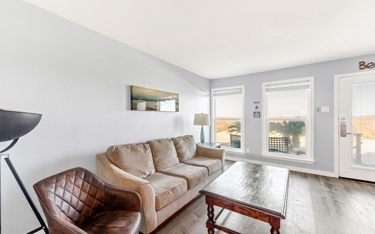 Relax in your bright living room with plush sofa, stylish leather chair, and peaceful patio views through large windows.