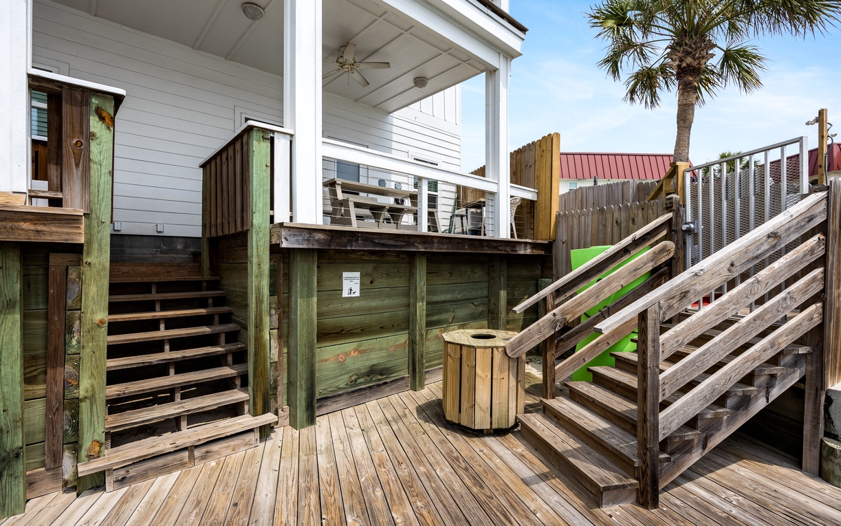 Your elevated deck features weathered wood railings and stairs, with tropical palms swaying above your beachside retreat.