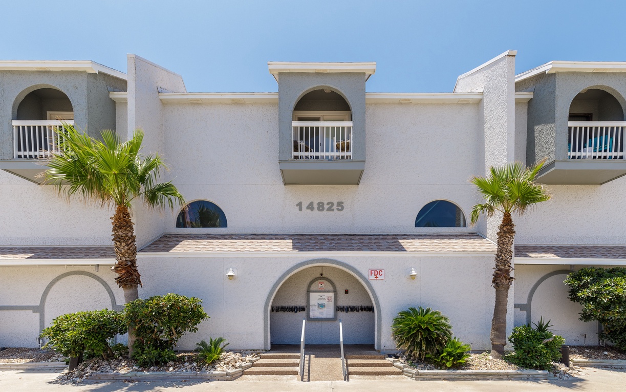 Mediterranean-style building with palm trees and distinctive arched balconies creates an inviting coastal retreat atmosphere.