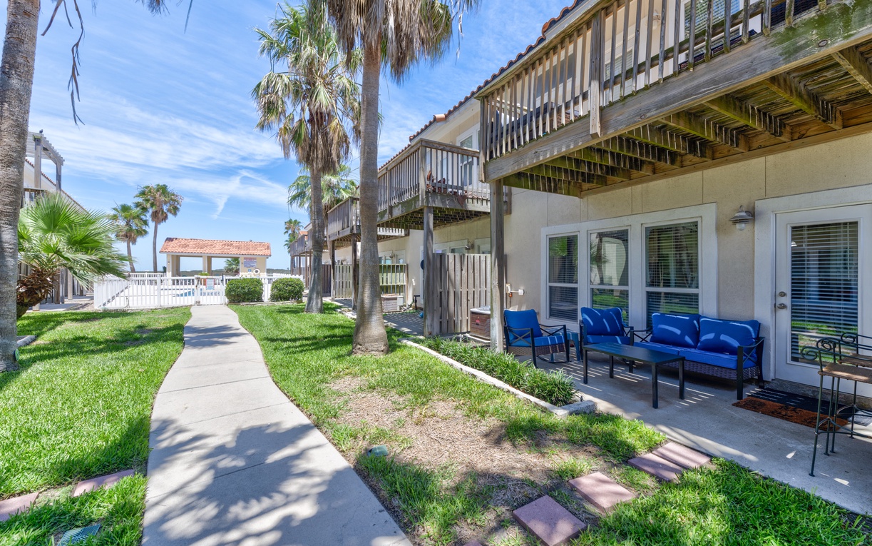 Coastal townhome complex featuring ground-floor patios, tropical landscaping with palm trees, and access pathways connecting neighboring beach residences.