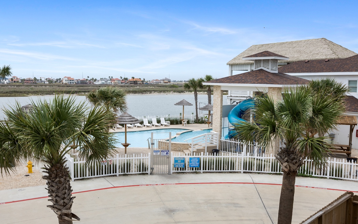 Waterfront resort featuring pool area with slides and lagoon views surrounded by palm trees.