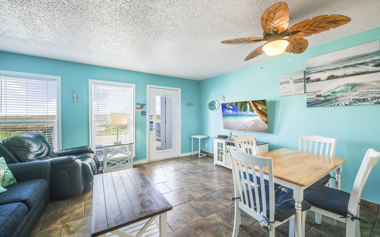 Step into your beach-themed retreat with turquoise walls, tropical ceiling fan, and cozy seating—perfect for unwinding after sun-soaked days with a view of the dunes just beyond your door.
