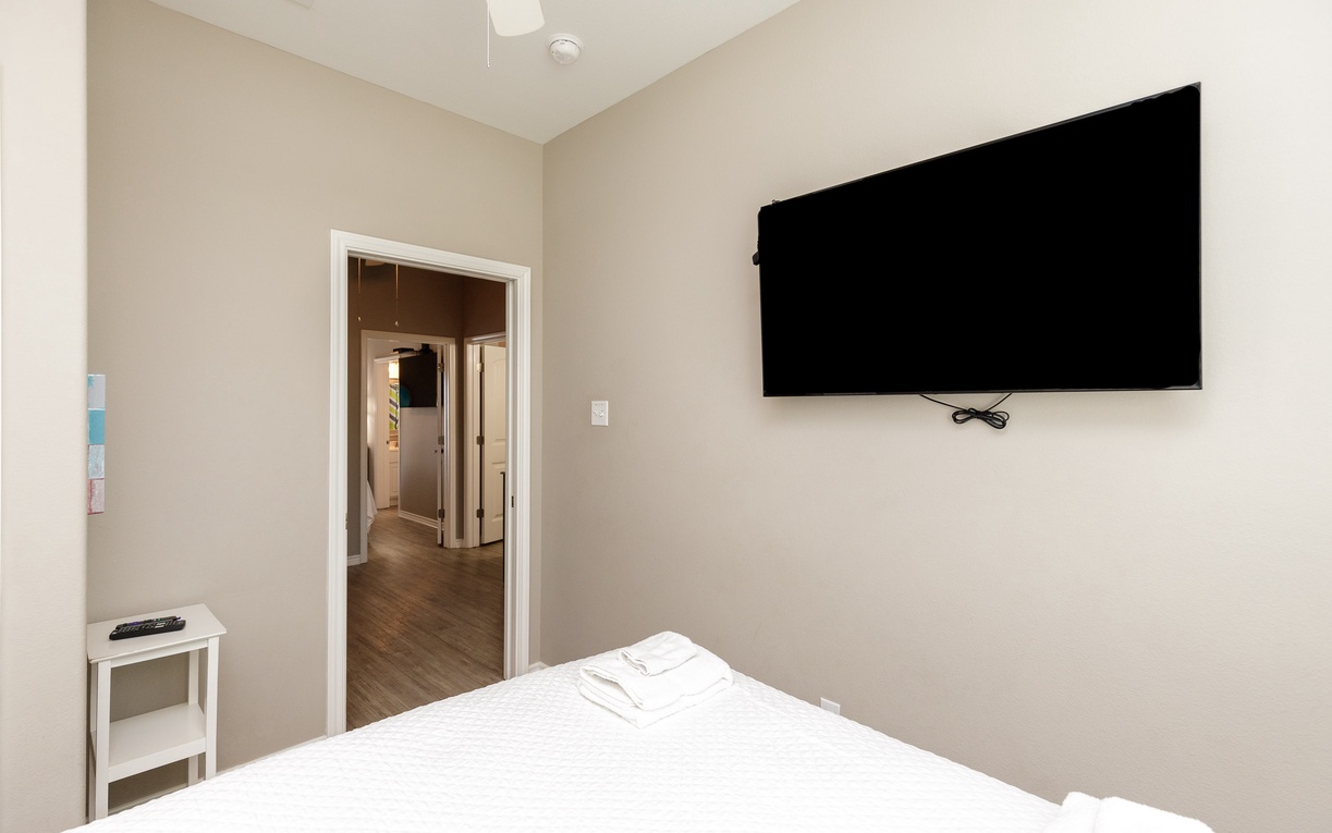 Unwind in your peaceful bedroom with crisp white linens and a large wall-mounted TV for cozy movie nights.