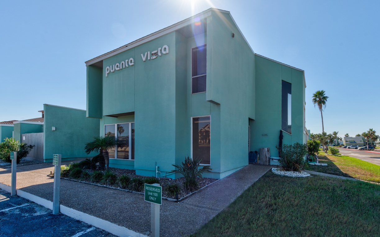 Modern turquoise property building with tropical landscaping and palm trees, featuring contemporary architecture in a sunny coastal setting.