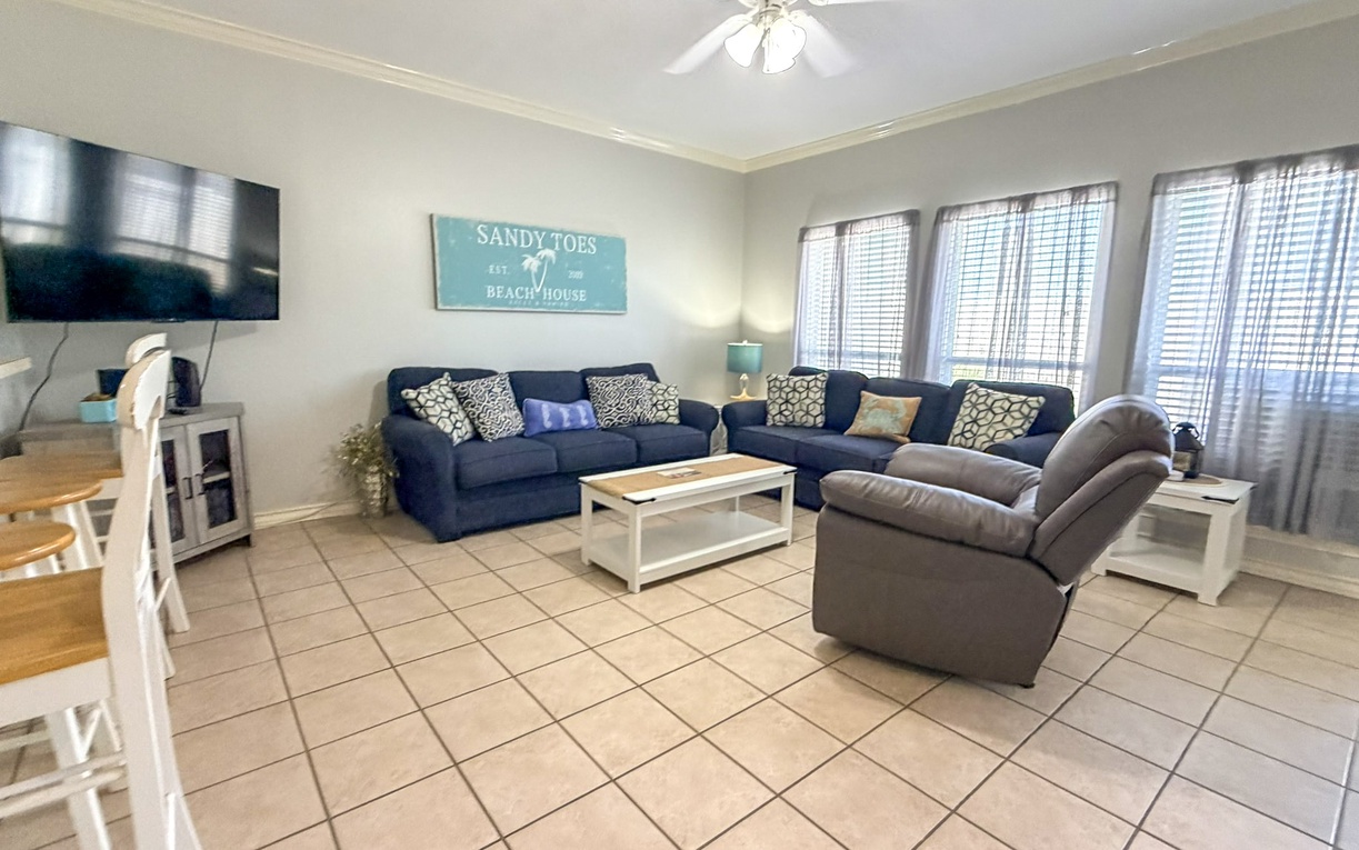 Relax in your spacious living room with comfy seating, beach-themed decor, and entertainment center for cozy vacation evenings.