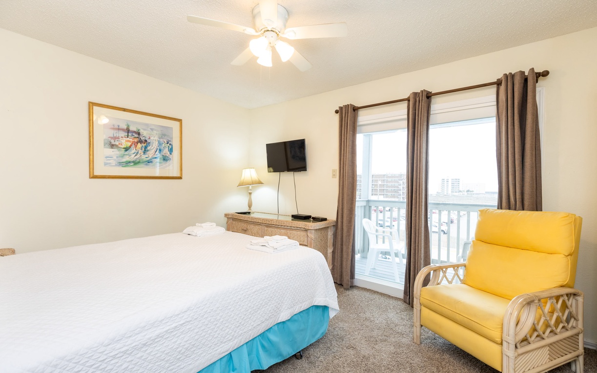 Relax in your bright bedroom featuring a comfy bed, cheerful yellow chair, and balcony access with lovely views beyond.