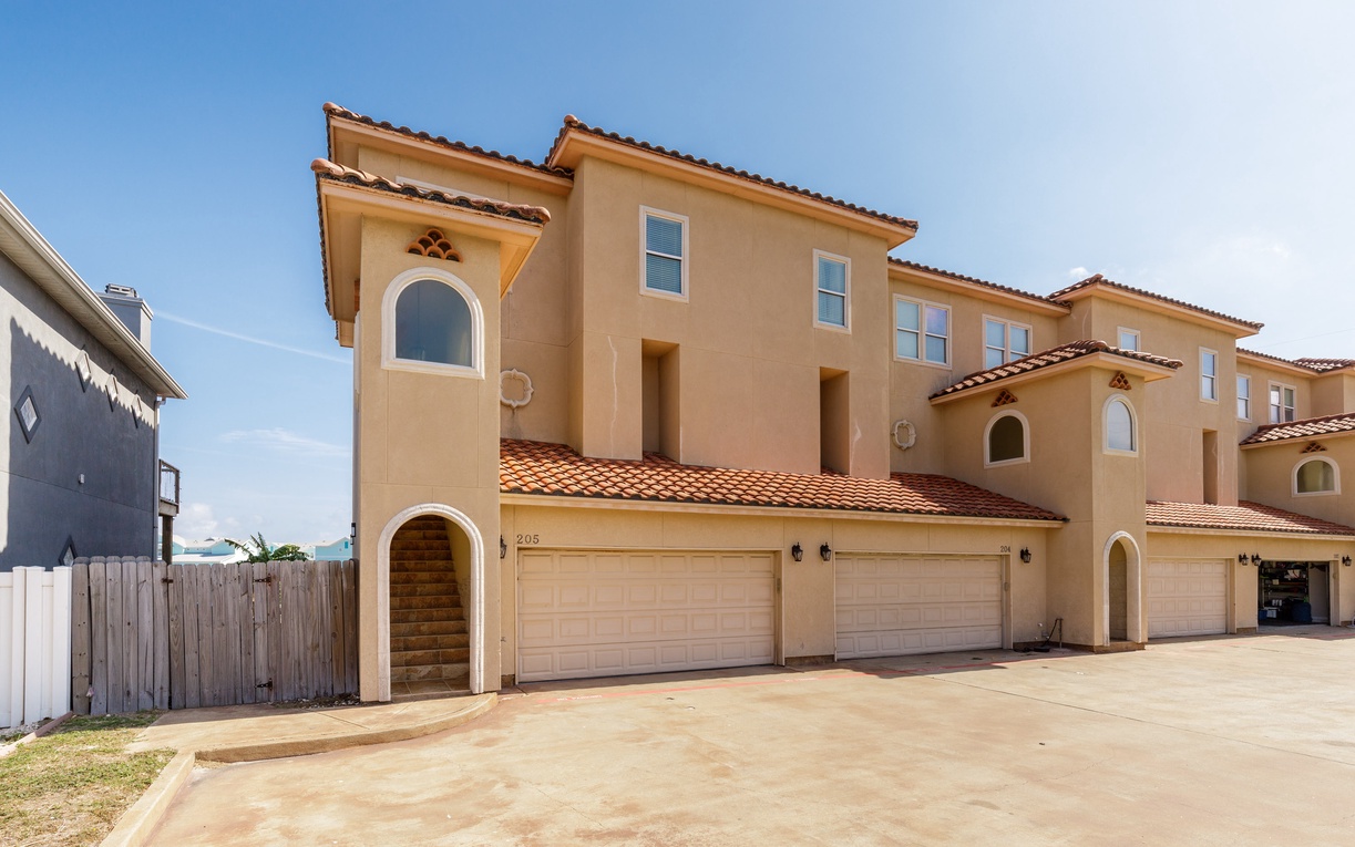 Mediterranean-style townhome complex with red tile roofing and convenient garage parking in a quiet residential area.