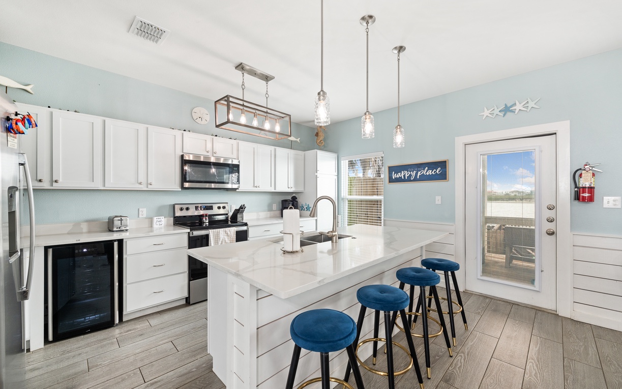 Step into your bright, coastal-inspired kitchen where soft blue tones and crisp white cabinetry set a serene mood. Gather around the spacious island with plush navy stools, perfect for morning coffee or planning your day's adventures.