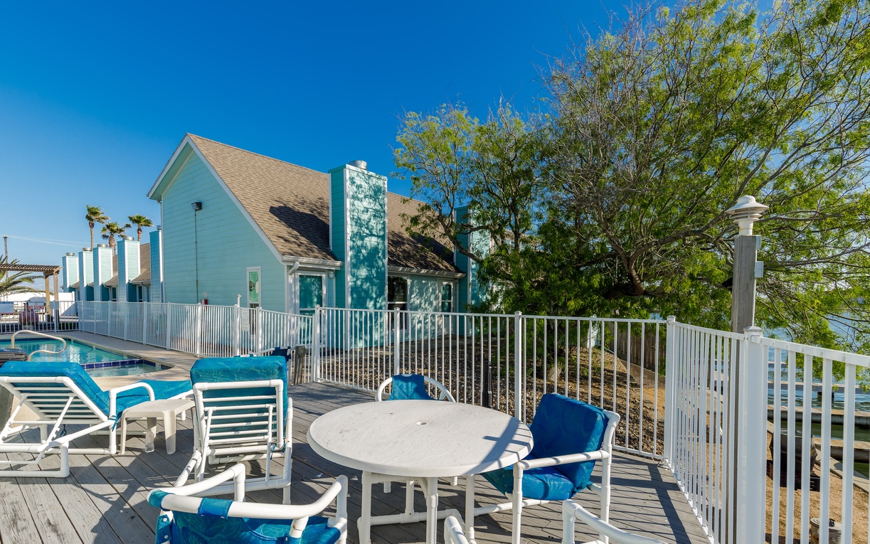 Relax on your private deck with outdoor dining and pool access, surrounded by tropical charm and clear blue skies.