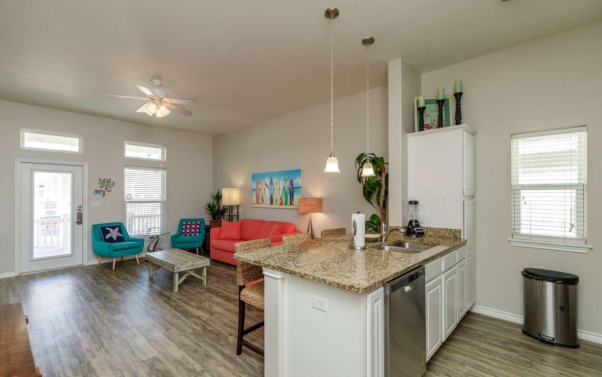 Relax in your bright, open-concept space featuring modern kitchen with granite counters and colorful living area with beach-themed décor.