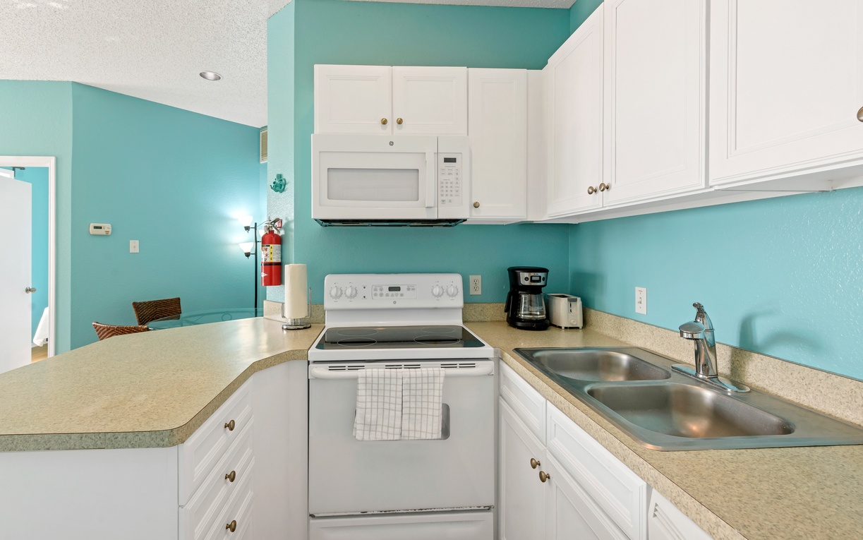 Your bright, fully-equipped kitchen awaits with white cabinets, modern appliances, and cheerful turquoise walls to inspire your culinary adventures.