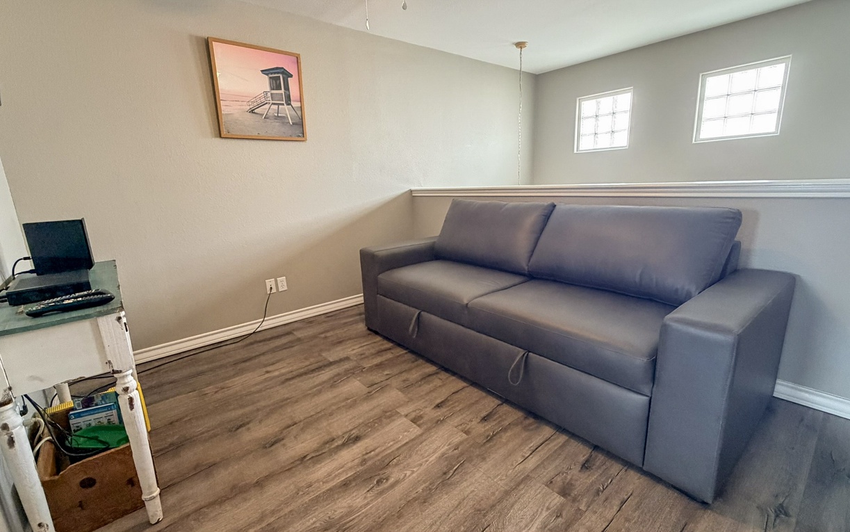 Your comfortable lounge space awaits with a plush sofa, work desk, and coastal-inspired artwork—perfect for unwinding or catching up on work in this bright, modern retreat.