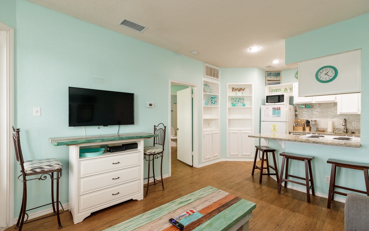 Unwind in your bright coastal living space with soothing mint walls, modern kitchen, and comfortable seating for relaxing after beach adventures.