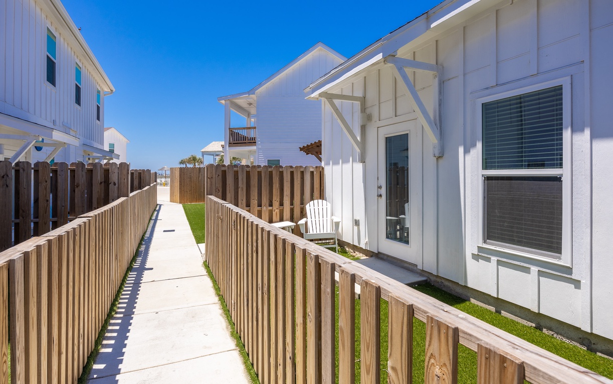 Modern coastal property with clean white exteriors and wooden walkway leading to your private entrance under clear blue skies.