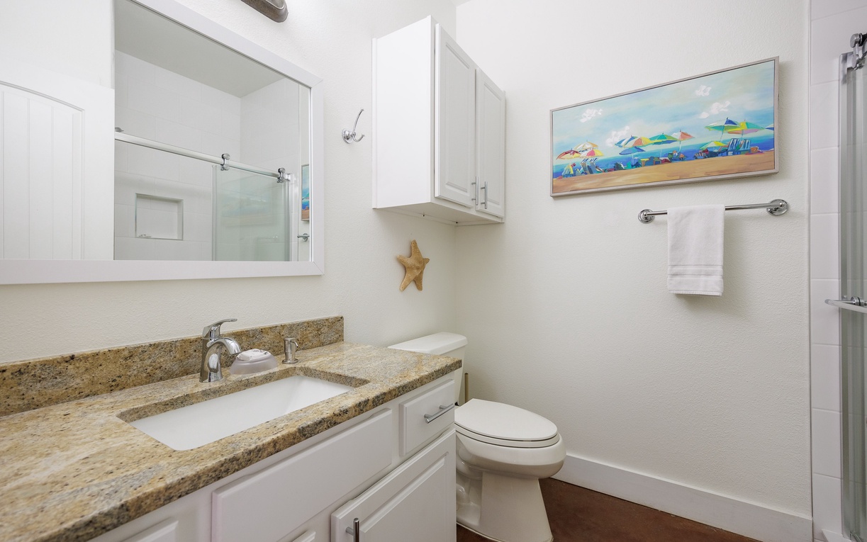 Refresh in your private bathroom featuring granite countertops, white cabinetry, and cheerful beach-themed artwork that sets a coastal mood.
