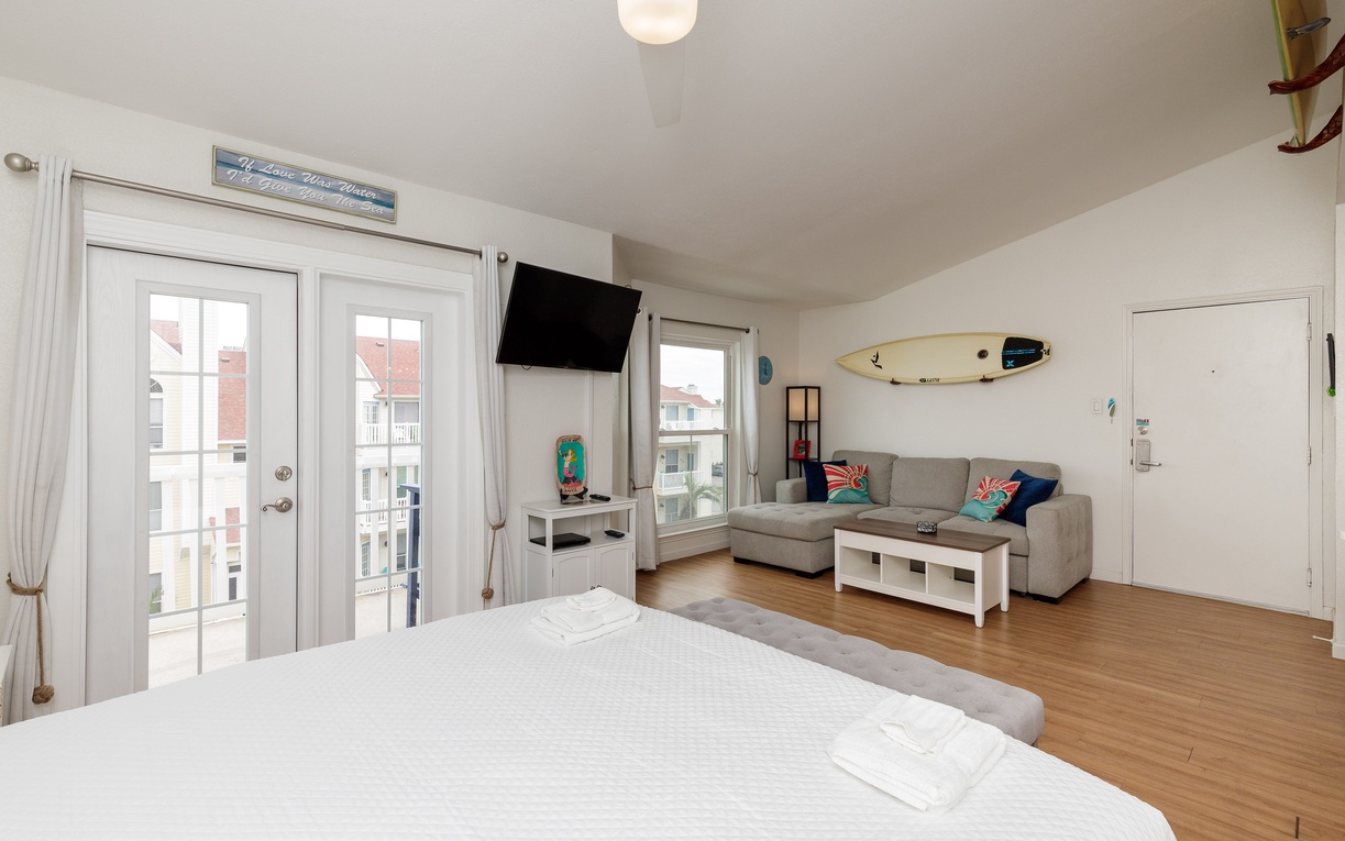 Your bright studio combines comfort and coastal charm with a cozy bed, sectional sofa, and surfboard accent that captures the beach spirit perfectly.