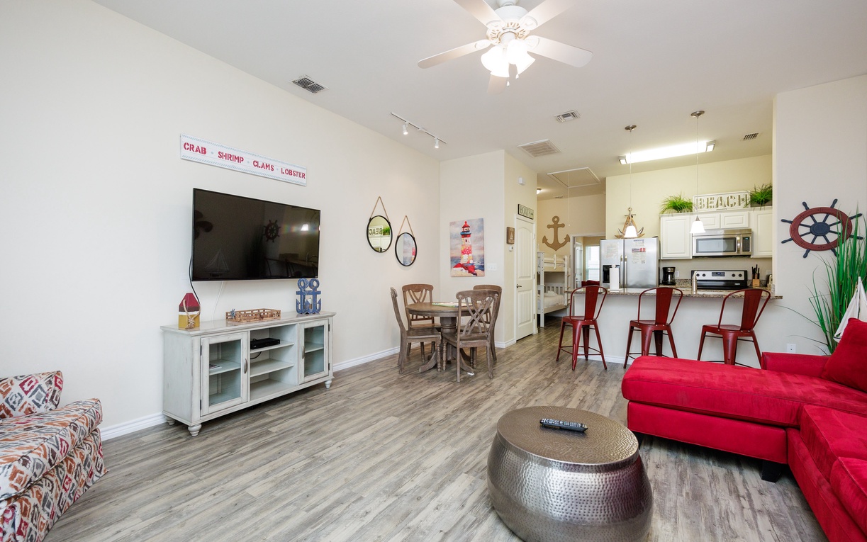 Your open-plan living space blends comfort and coastal charm, featuring a bright red sectional, entertainment center, and nautical touches throughout.