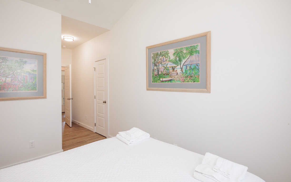 Unwind in your bright, peaceful bedroom with crisp white linens and charming tropical artwork creating a serene retreat.