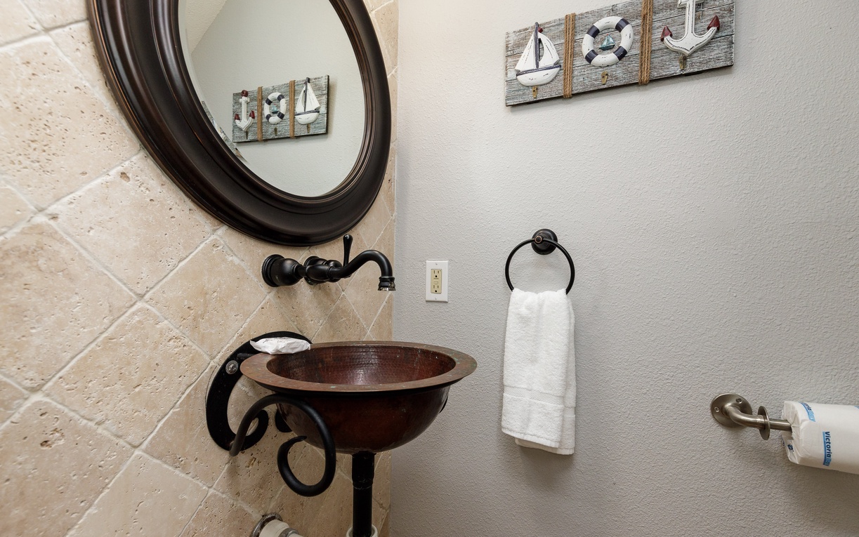 Freshen up in your charming nautical-themed powder room, featuring a unique copper vessel sink and coastal décor.