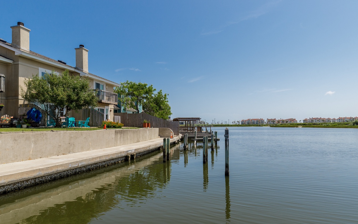 Waterfront property with private dock on calm waters, surrounded by residential neighborhood under clear blue skies.