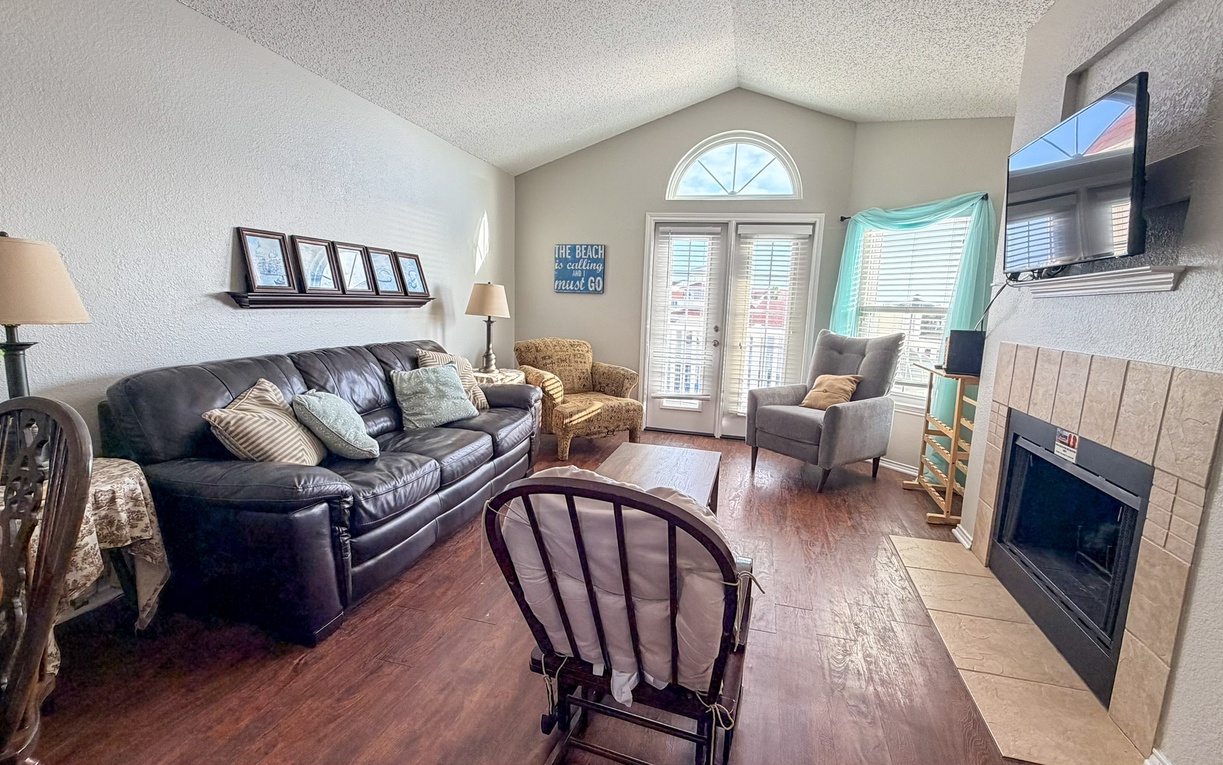 Unwind in your cozy living room with leather seating, warm fireplace, and beach-themed charm. Natural light streams through French doors to create your perfect retreat.