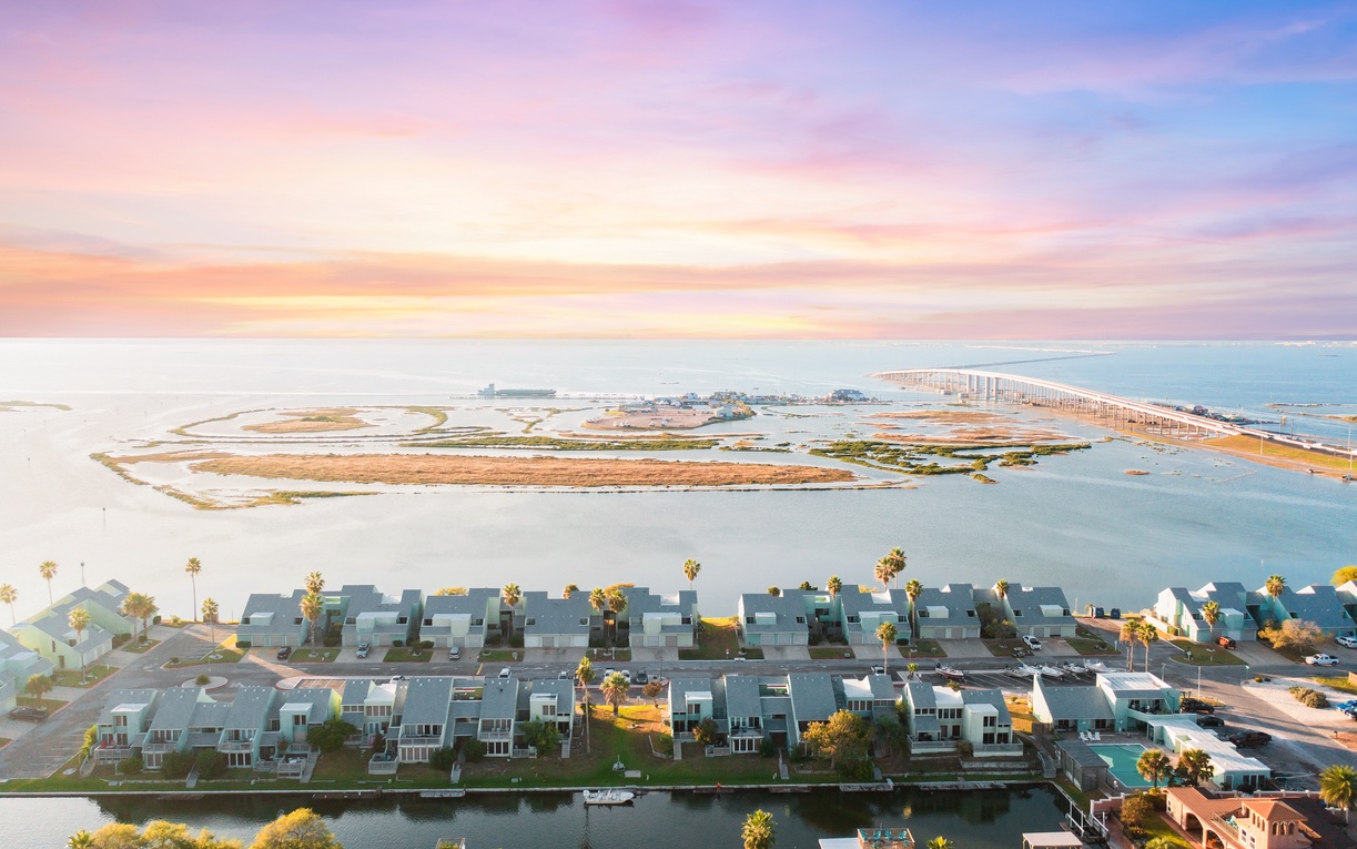 Stunning aerial view showcases the waterfront community and scenic bridge spanning across tranquil waters under a breathtaking sunset sky.