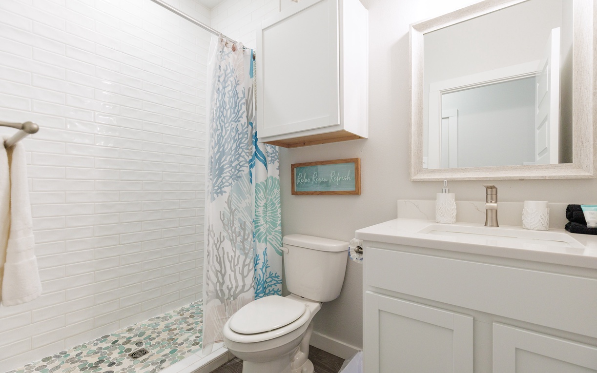 Freshen up in this bright coastal bathroom featuring a tiled shower, modern vanity, and charming ocean-themed decor.
