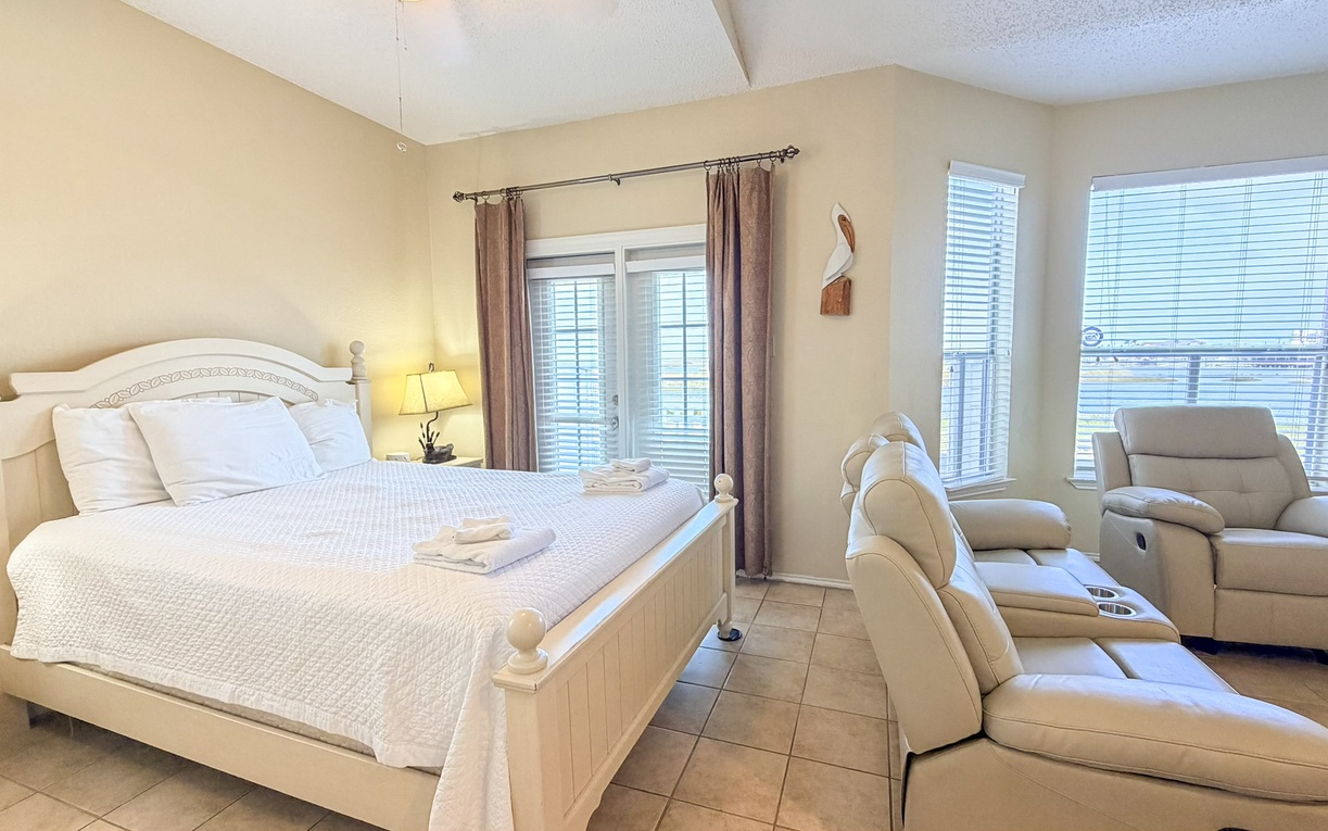 Relax in your spacious bedroom with plush reclining chairs and a comfortable bed, perfectly positioned for morning light through multiple windows.