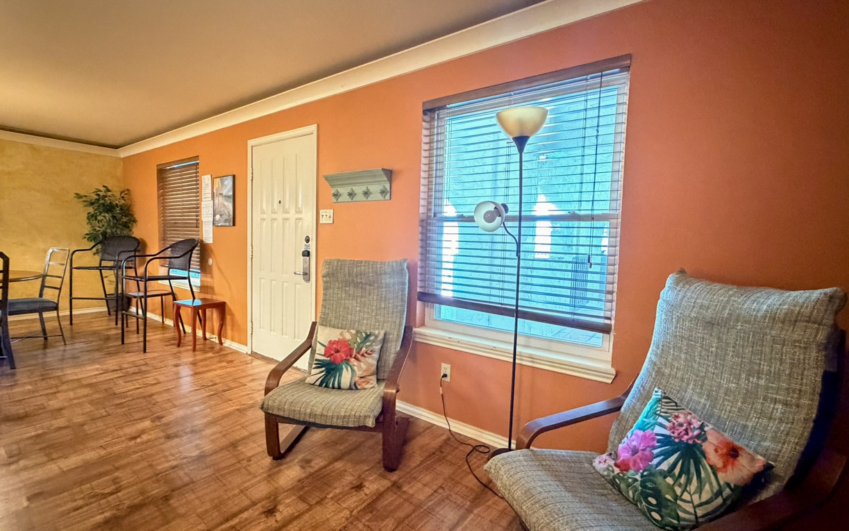 Relax in your vibrant living space with comfy chairs, tropical accents, and warm natural light streaming through large windows.