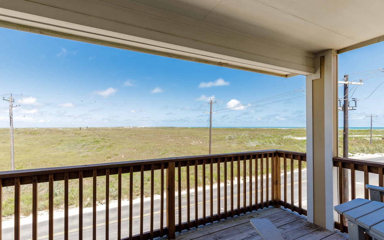 Covered balcony overlooking expansive coastal grasslands and open sky with distant ocean views.