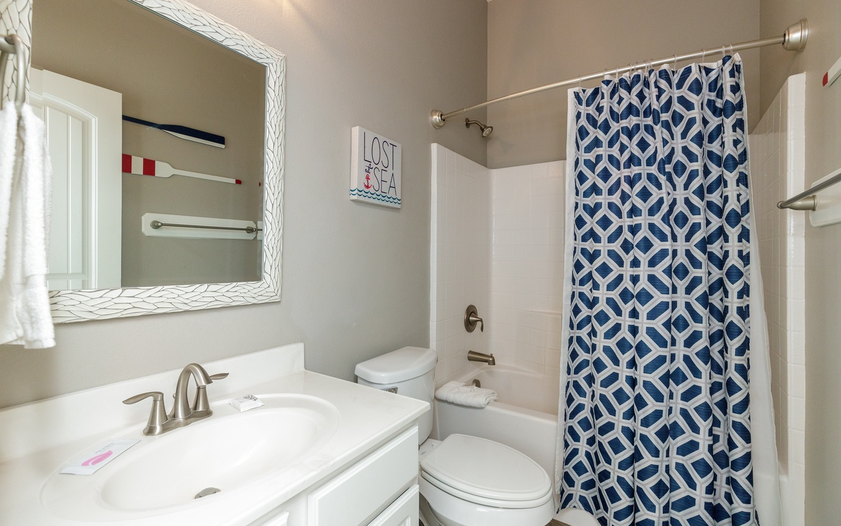 Step into your nautical-themed bathroom featuring a stylish blue geometric shower curtain and elegant white vanity with convenient storage.
