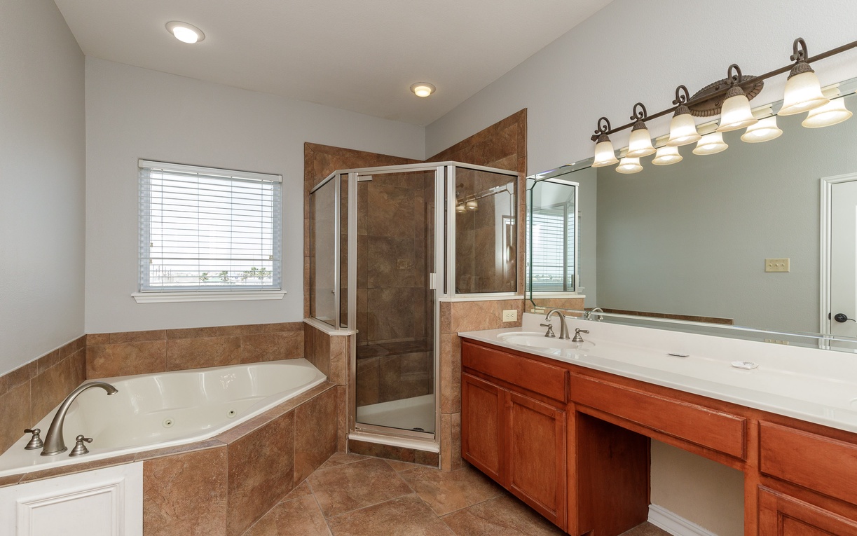 Indulge in your spacious master bathroom with a jetted corner tub, separate glass shower, and elegant vanity lighting for pure relaxation.