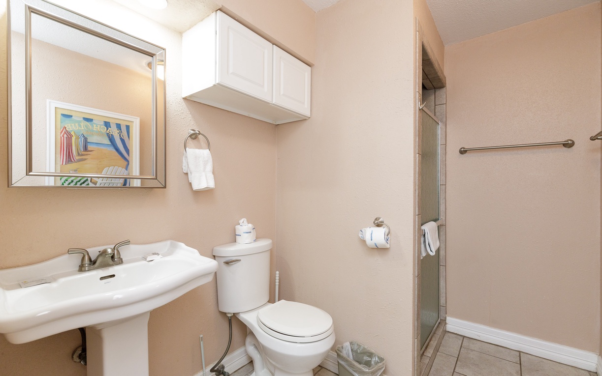 Step into your private bathroom with walk-in shower, pedestal sink, and thoughtful touches like fresh towels and coastal artwork.