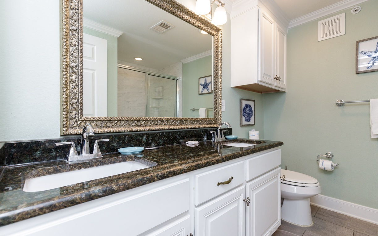 Step into your elegant bathroom featuring granite countertops, a gold-framed mirror, and coastal artwork that creates a spa-like retreat.