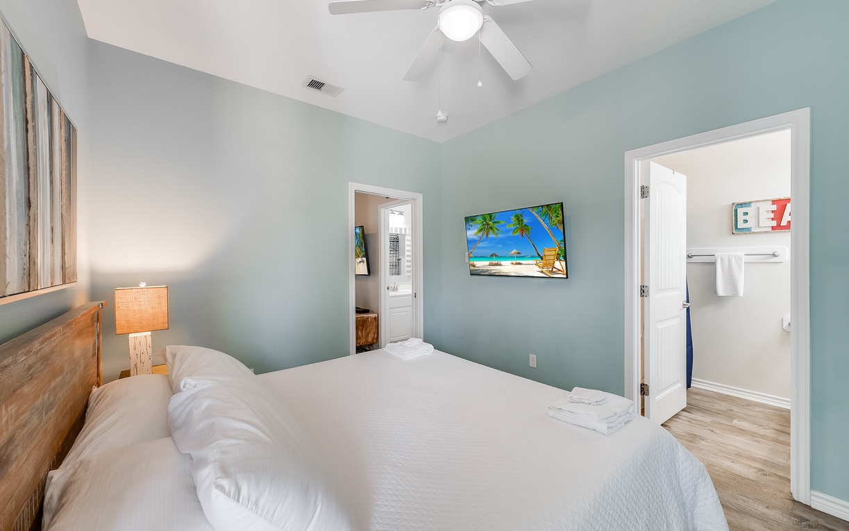 Wake up refreshed in your cozy bedroom with calming seafoam walls, crisp linens, and tropical artwork setting a peaceful mood.
