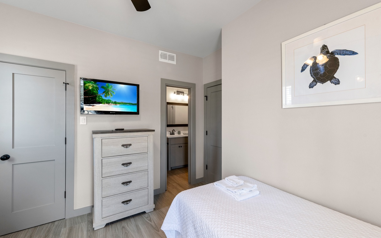 Your cozy bedroom features a comfortable bed, wall-mounted TV for entertainment, and charming sea turtle artwork creating a peaceful coastal retreat.