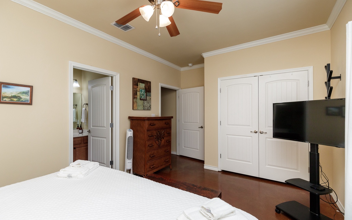 Unwind in your spacious bedroom featuring a ceiling fan, flat-screen TV, and elegant wood furnishings for your perfect retreat.