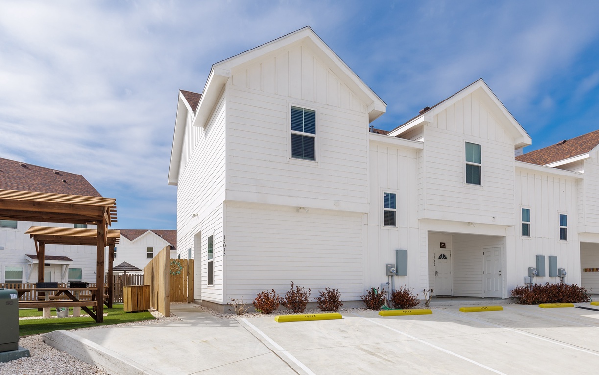 Modern white townhome complex featuring spacious two-story units with contemporary design and convenient parking spaces.