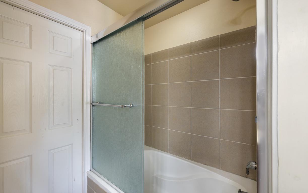 Freshen up in your private bathroom featuring a deep tub and spacious walk-in shower with rainfall showerhead, all framed by sleek neutral tile.