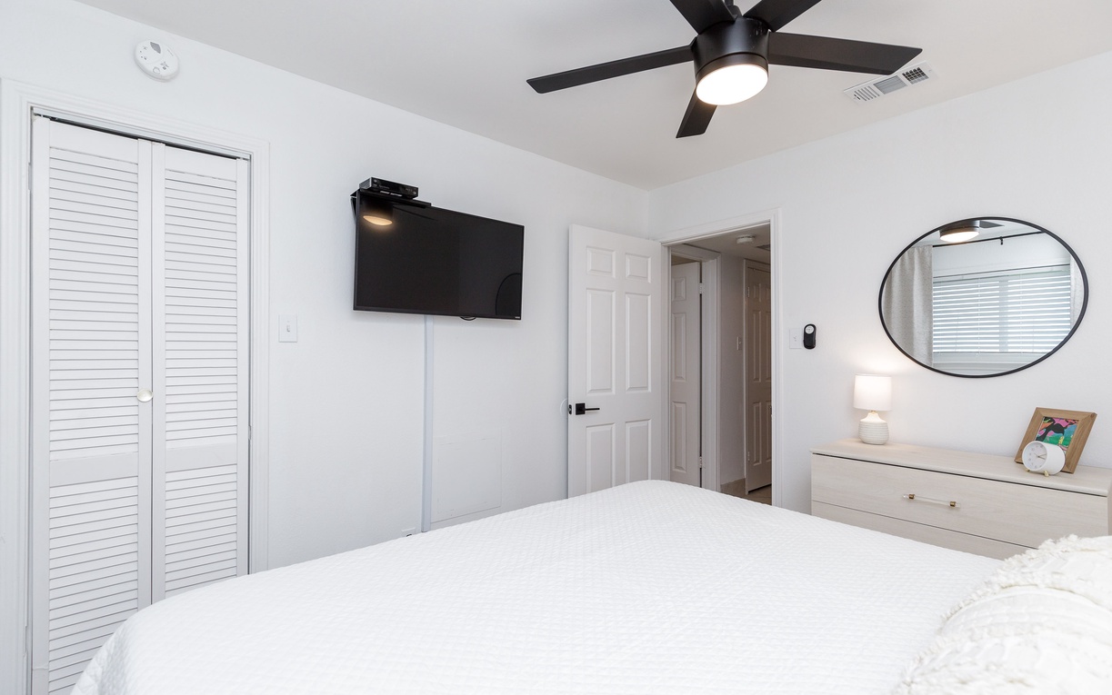 Unwind in your bright bedroom with crisp linens, ceiling fan, wall-mounted TV, and thoughtful touches like the bedside lamp for ultimate comfort.