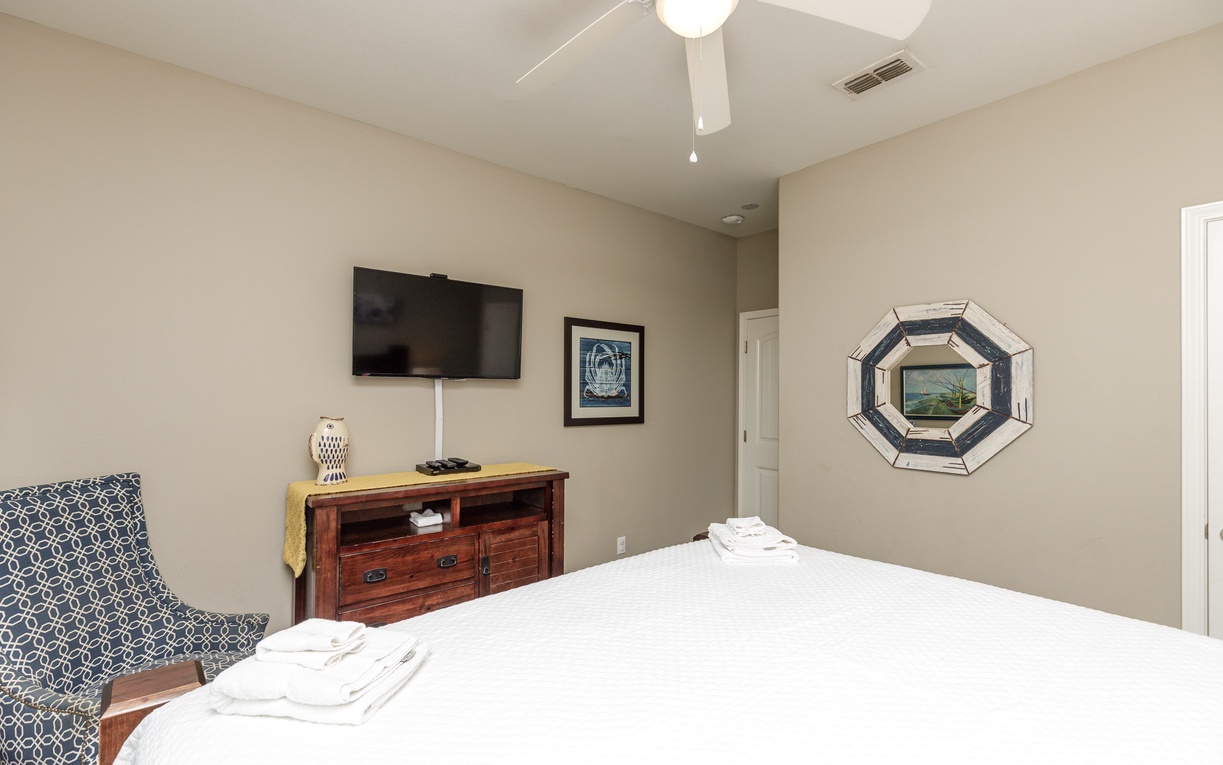 Unwind in your peaceful bedroom with a cozy armchair, ceiling fan, and entertainment center—everything you need for restful nights.