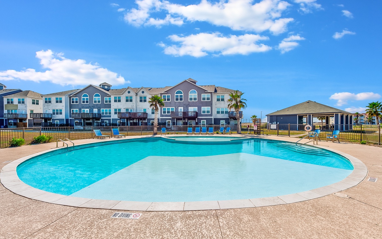 Large community pool with crystal-clear water surrounded by comfortable lounge chairs, perfect for sunny days of relaxation.