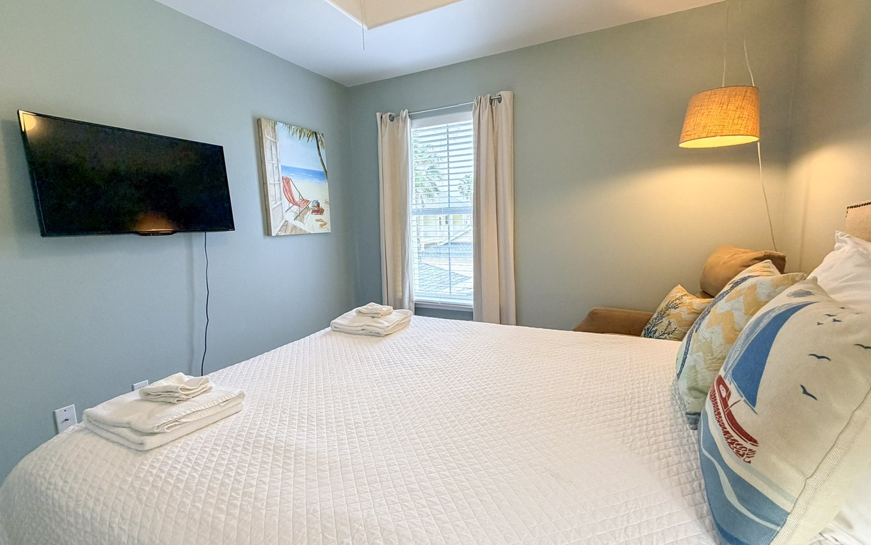 Unwind in your peaceful bedroom with calming blue walls, crisp white linens, and a wall-mounted TV for cozy evenings.