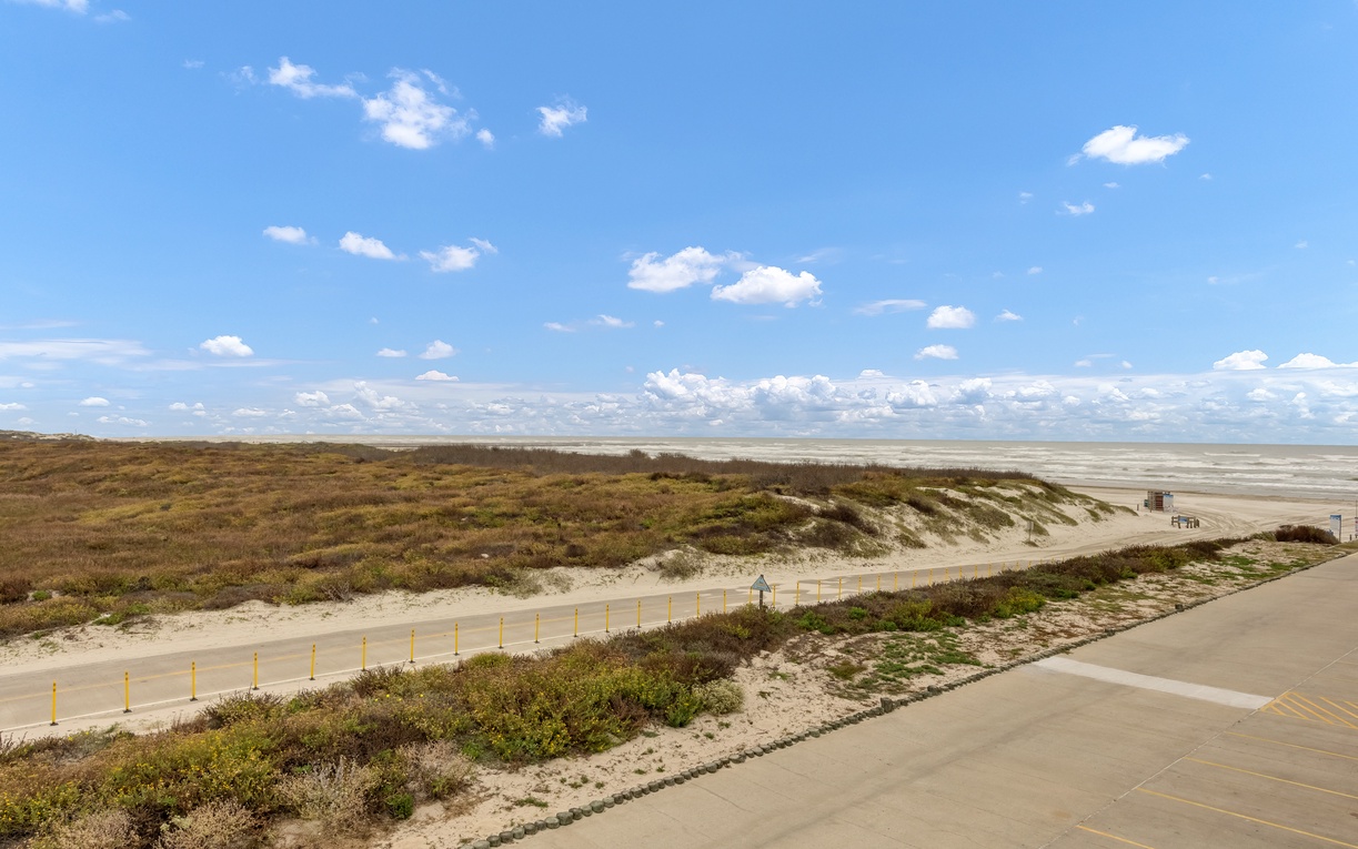 Coastal dunes and beach access area with natural vegetation and sandy pathways leading to the shoreline.