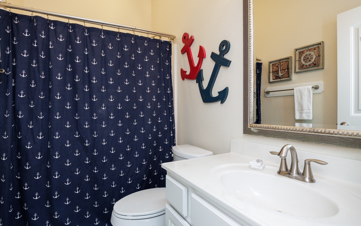 Step into your charming nautical-themed bathroom featuring playful anchor décor and crisp white fixtures for a refreshing coastal retreat.