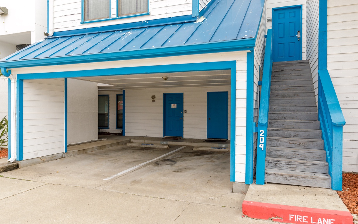 Covered parking spaces and stairway access provide convenient arrival at this charming blue and white coastal building.
