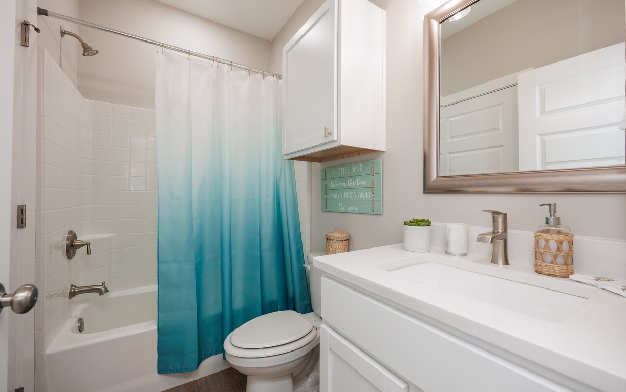 Your bright bathroom features a relaxing shower-tub combo with cheerful ombre curtain and thoughtful amenities for your comfort.